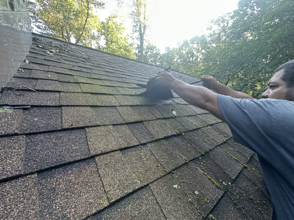 detailed photo of a MI Homesiding & Roofing contractor installing bright metal step flashing interlayered with shingles around a Knoxville chimney.