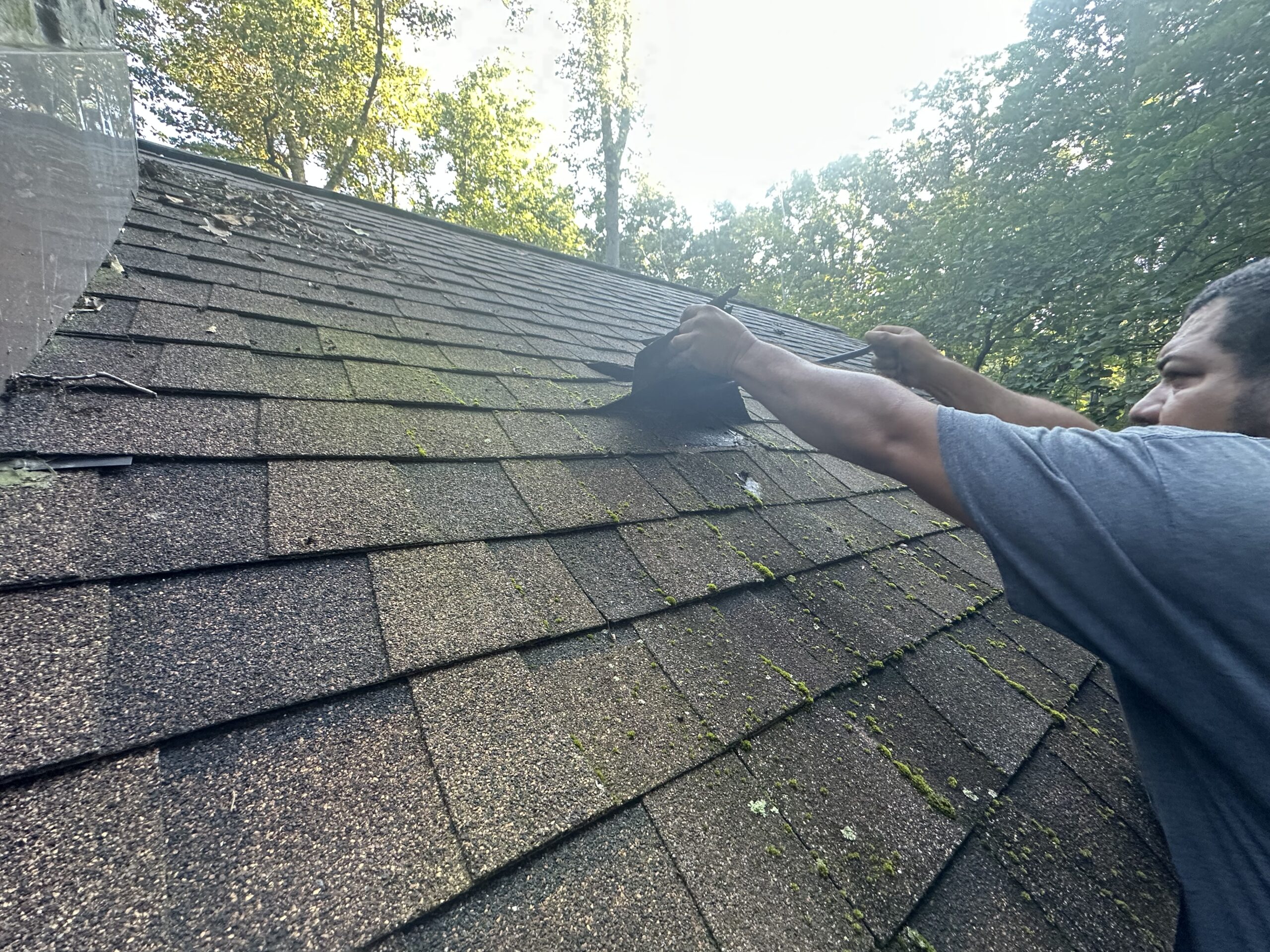 detailed photo of a MI Homesiding & Roofing contractor installing bright metal step flashing interlayered with shingles around a Knoxville chimney.