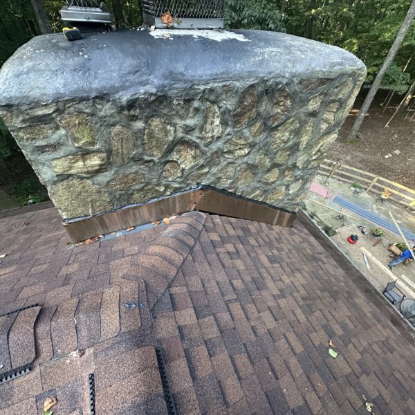 Stone chimney with new copper flashing where it meets a shingle roof