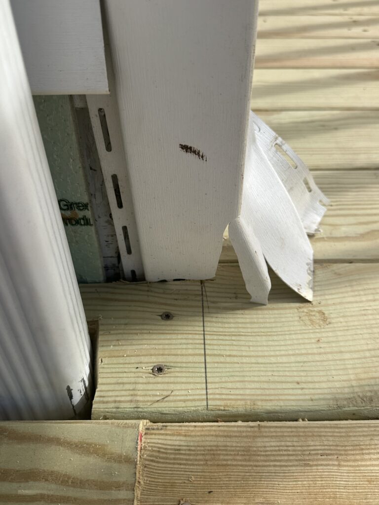 Close-up of a dangerous deck ledger board pulling away from a Knoxville house siding, showing rusted nails and rotting wood.