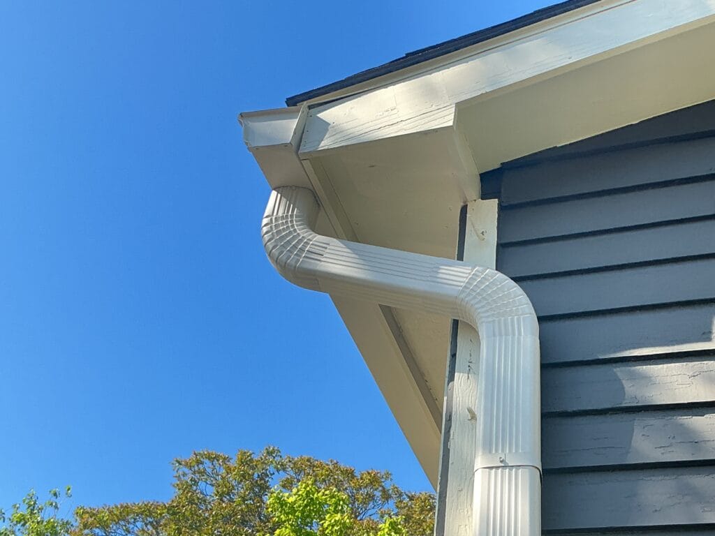White gutter and downspout elbow at the corner of a navy blue lap siding home in Knoxville, TN