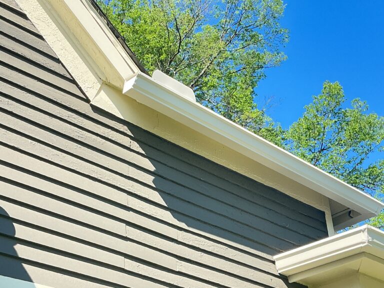 omparative technical photo on a Knoxville TN home showing a new, continuous pre-painted white seamless aluminum gutter from MI Homesiding LLC on the left, contrasting sharply with an old, leaking, multi-seamed sectional white aluminum gutter on the right.