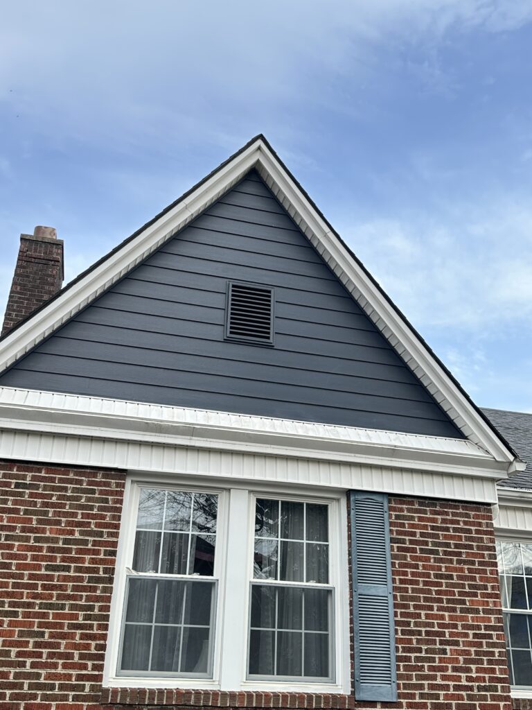 Exterior view of a home showing a technician sealing a new energy-efficient window that is perfectly integrated with the new fiber cement siding panels.