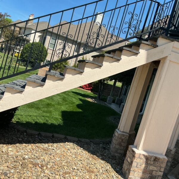 Exterior staircase with an iron railing and stone columns on a landscaped lot