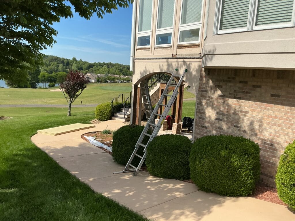 Extension ladder at a covered entry during exterior work on an East Tennessee home, with the lake behind