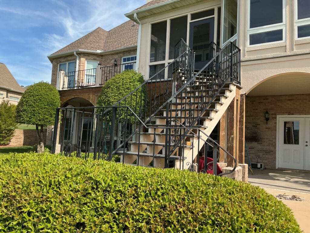 Elevated screened porch with ornamental iron stairs and new structural posts during an exterior rebuild