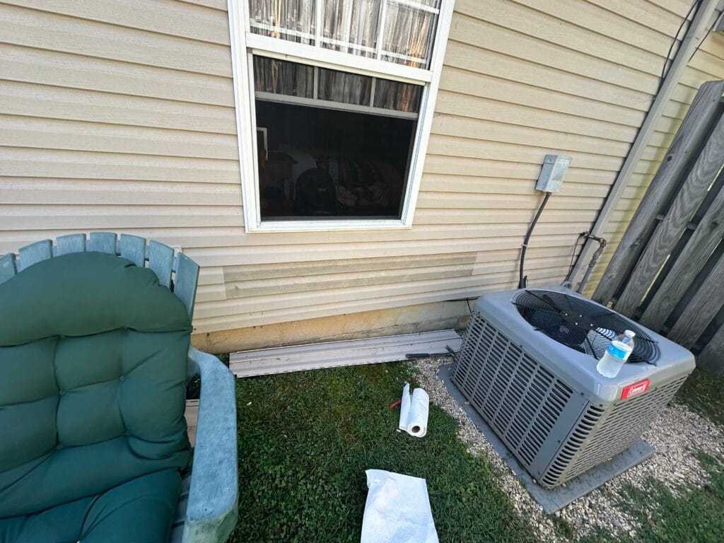 Vinyl siding with staining along the lower courses and replacement pieces staged on the grass