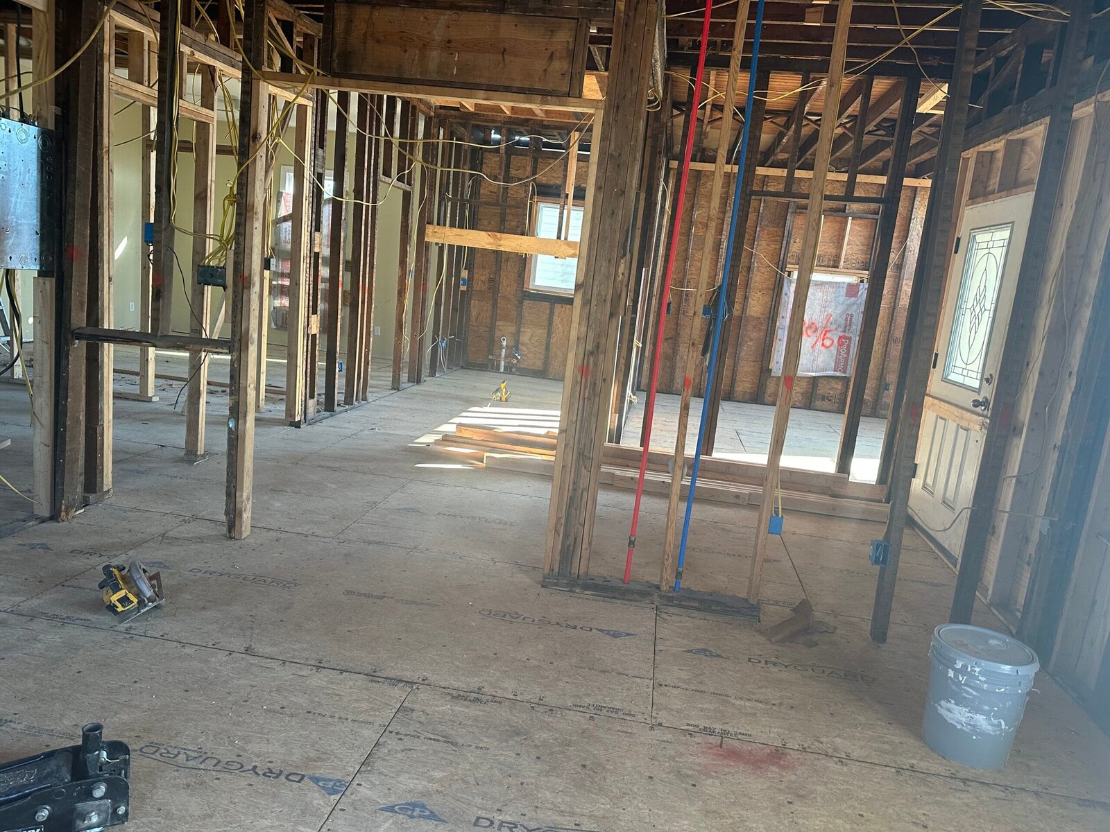 Interior of a home opened back to the studs during a project, with the wall framing, the sheathing and the plumbing and electrical runs exposed