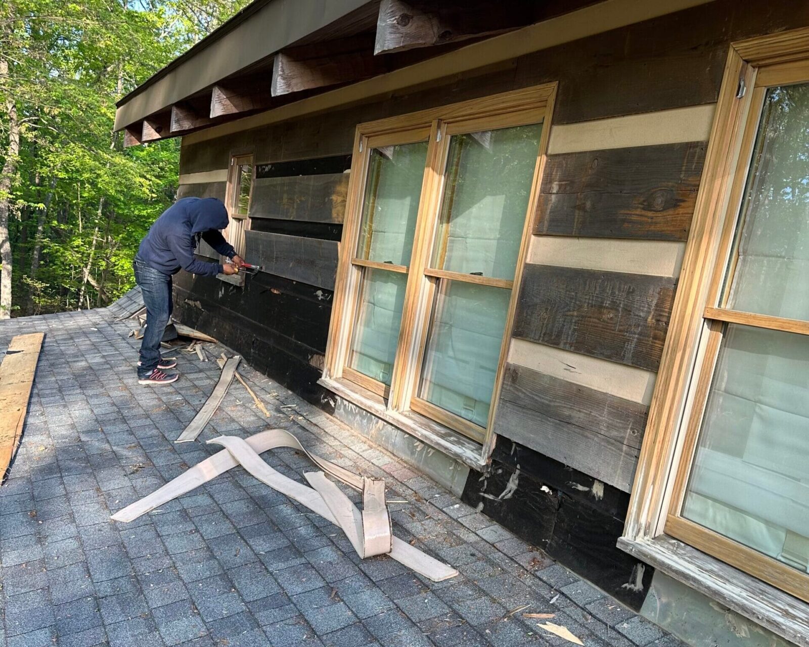 MI worker replacing weathered wood lap siding on a dormer wall above a shingle roof