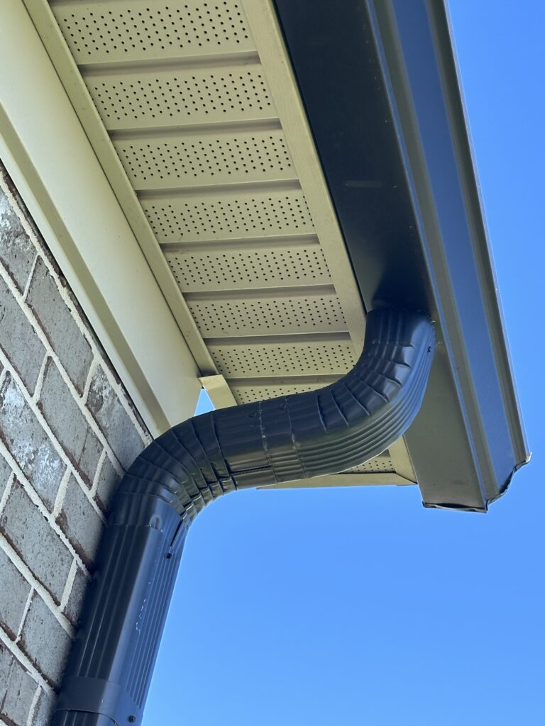 A detail photograph revealing the failure of a quick DIY repair attempt on a Knoxville home, where an insecurely fastened oversized bracket is pulling a weathered gutter further away, exposing the correct hidden hangers installed by MI Homesiding LLC nearby.