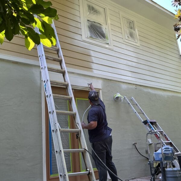 Painter using an airless sprayer from a ladder on a cream home in Knoxville, TN