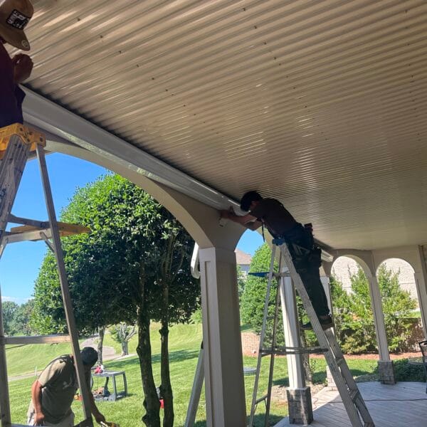 Installer on a ladder fitting white soffit panels under a porch ceiling in Knoxville, TN