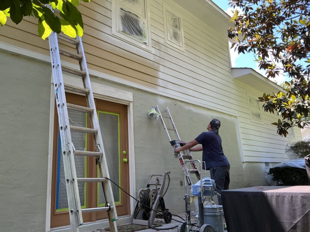 MI Homesiding painter spraying exterior paint from a ladder on a Knoxville, TN home
