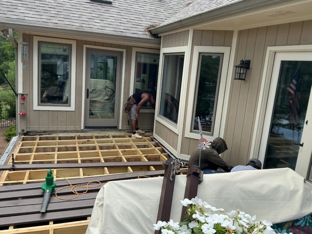 New pressure-treated joists laid out on a deck replacement beside a sunroom, with the first composite boards already down