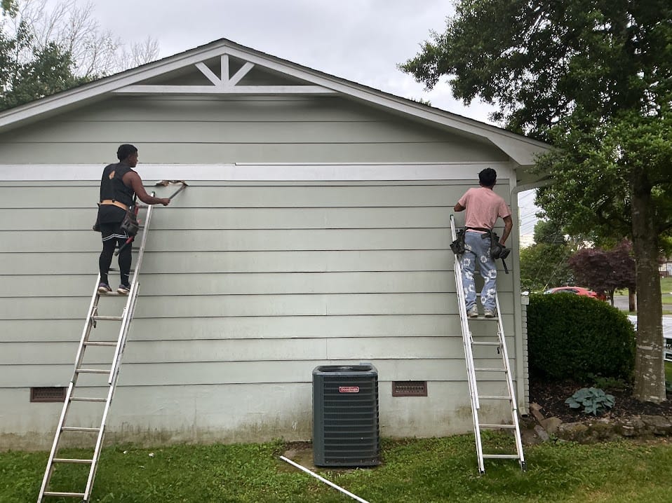 Two installers working on aged pale green lap siding at the gable of a ranch-style home