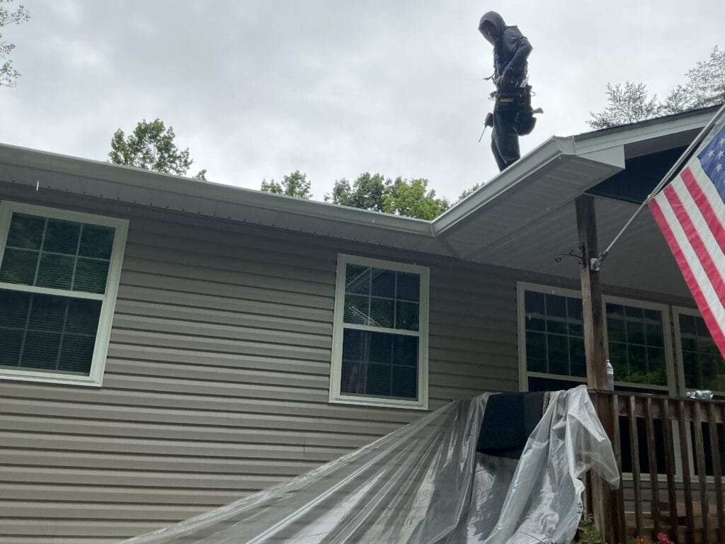 Installer standing at the roof edge above a newly fitted gutter on a ranch home, with the deck below sheeted over