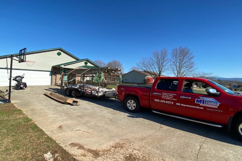MI Homesiding & Roofing truck and equipment trailer parked at a Knoxville, TN home with the old siding stripped off