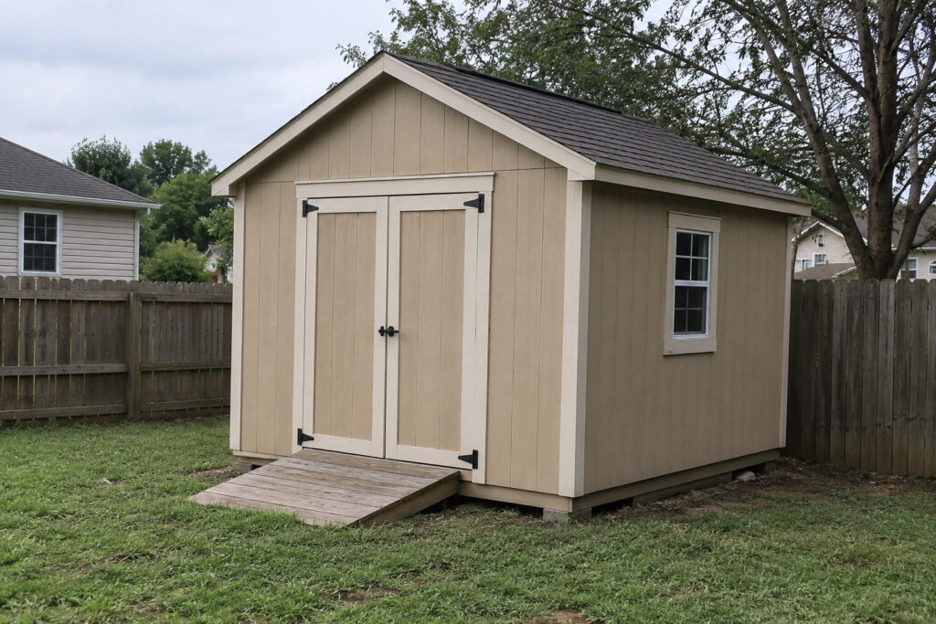 Completed backyard storage shed with double doors, a side window, a shingled gable roof and a wooden ramp at the doorway