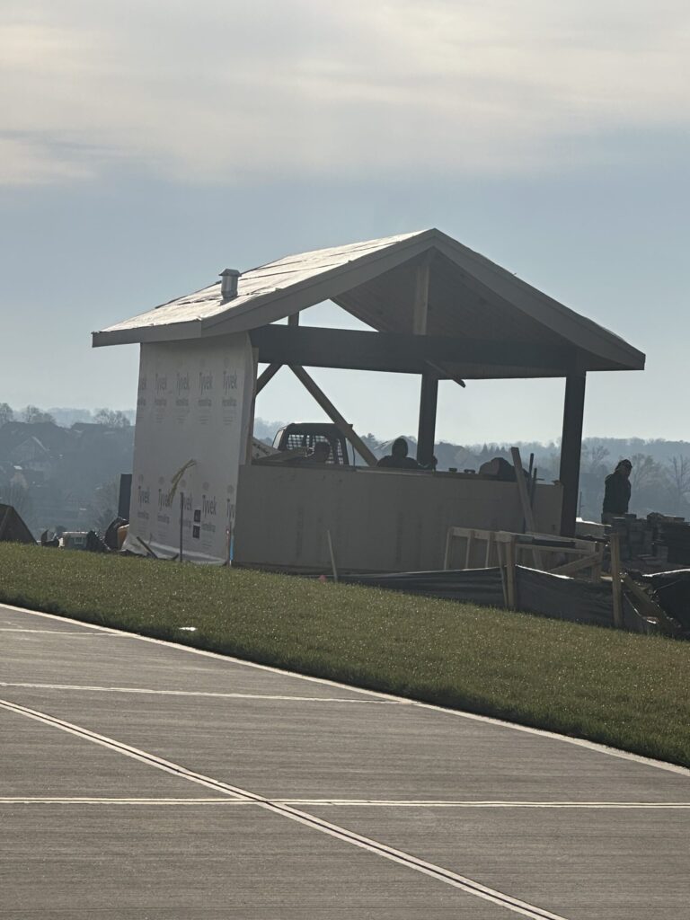 Small open-sided structure under construction, with post-and-beam framing, knee braces and roof underlayment in place