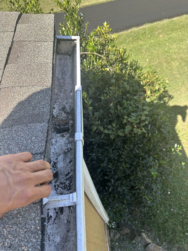 Hand clearing silt and grime from inside a gutter at the roof edge during a gutter cleaning in Knoxville, TN